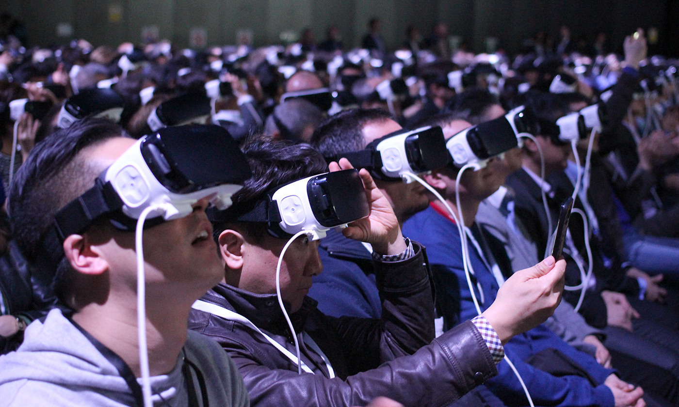 People use VR in an auditorium room [(source)](https://commons.wikimedia.org/wiki/File:Samsung%27s_Virtual_Reality_MWC_2016_Press_Conference_(26666393696).jpg).